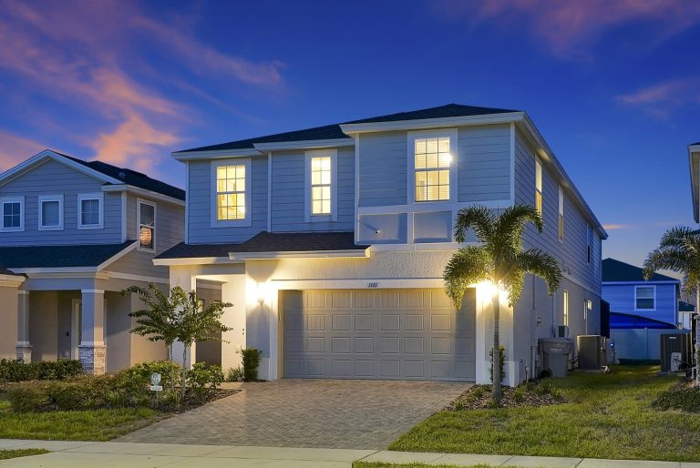 Two-storey house with lit windows and palm trees at dusk.