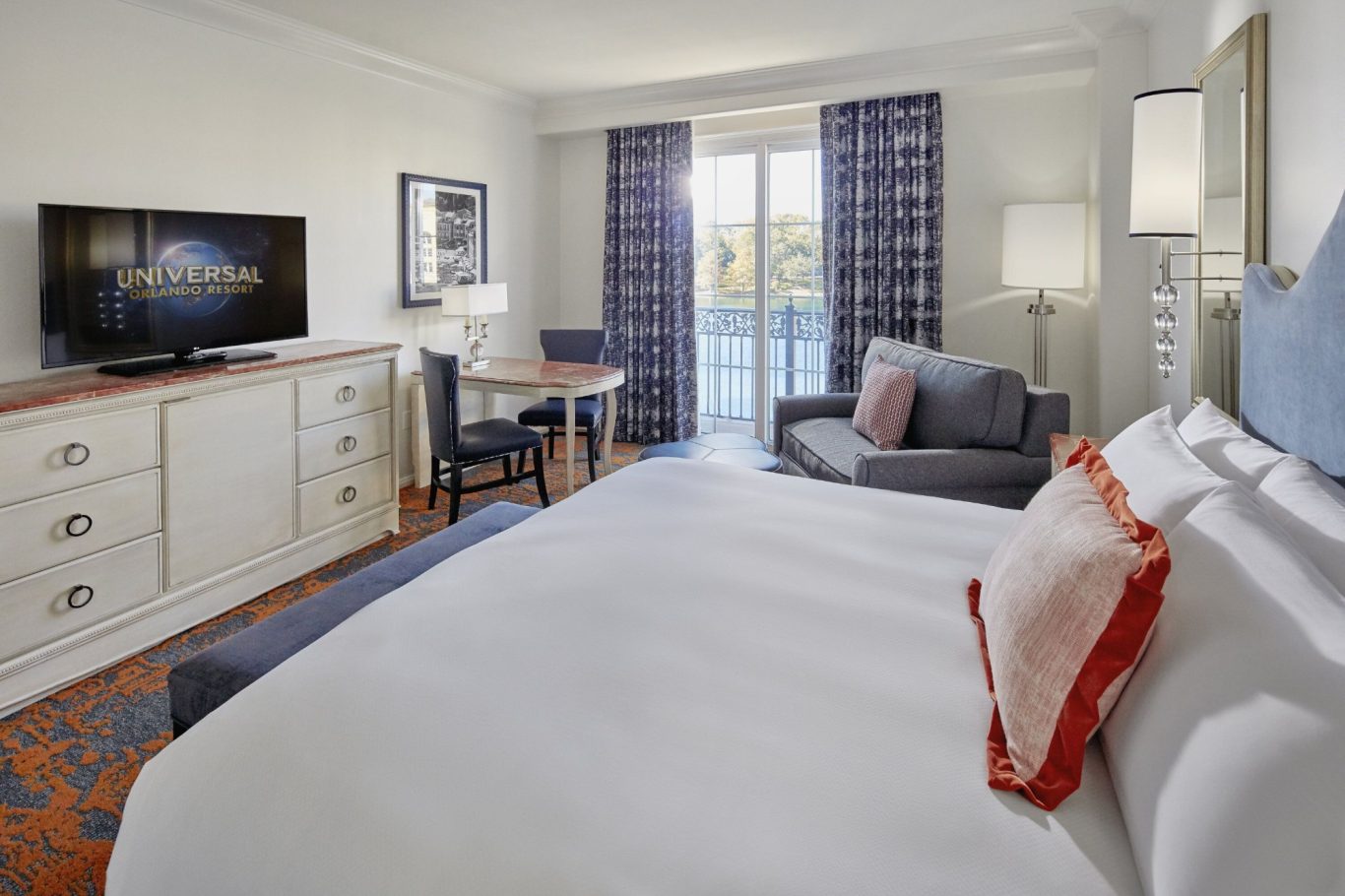 Modern hotel room featuring a bed, TV, seating area, and balcony access.