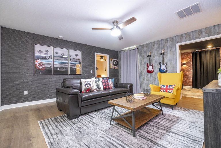 Modern living room with a black sofa, yellow armchair, and wall-mounted guitars.