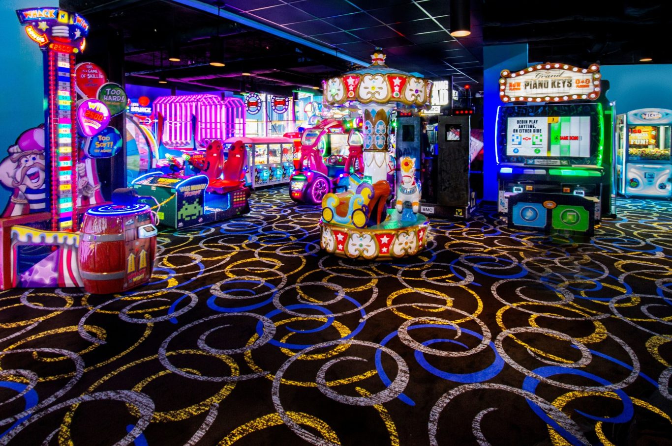 Colourful arcade with various games and bright lighting on a patterned carpet.