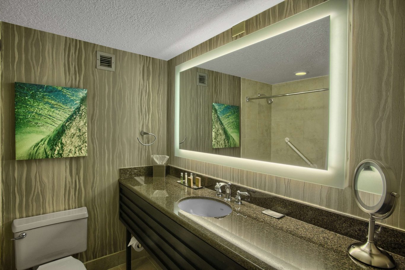 Modern bathroom featuring a sleek vanity, illuminated mirror, and a green landscape artwork.