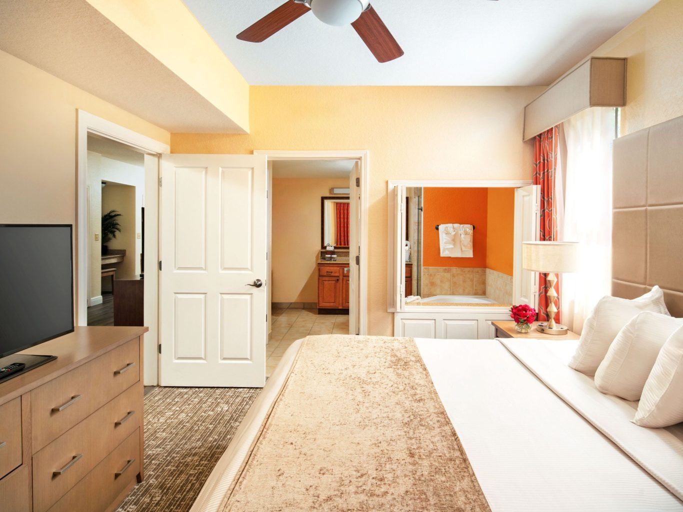 Bright hotel room featuring a bed, TV, and adjoining bathroom. Warm colours and natural light.