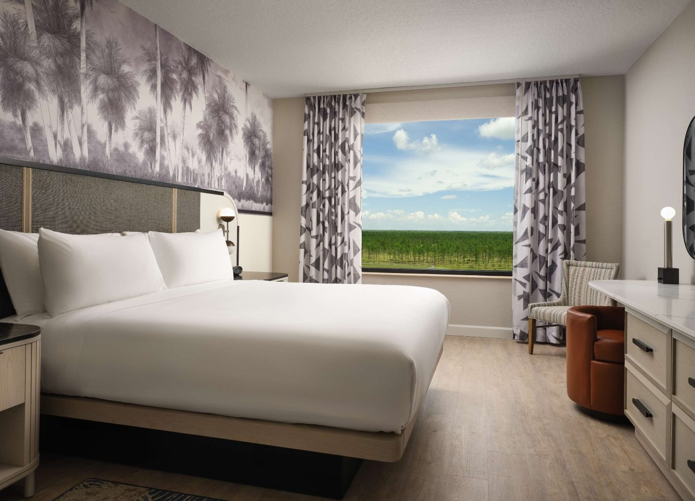 Modern hotel room featuring a large bed, desk, and window with a green landscape view.