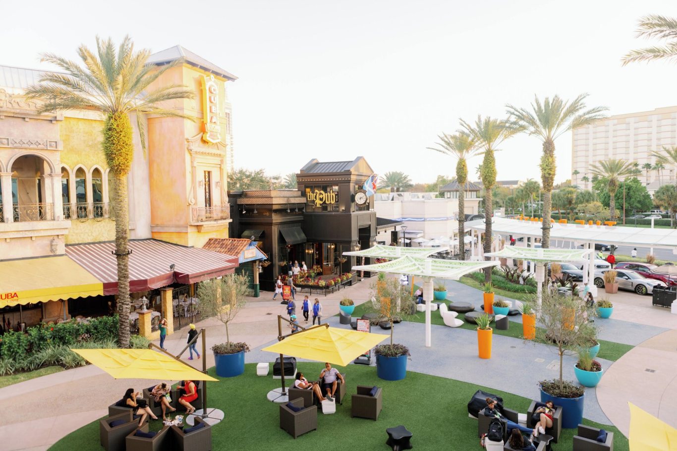 Outdoor dining area with palm trees, seating, and people enjoying a sunny day.