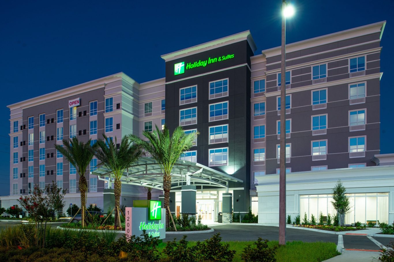 Modern hotel building with palm trees, illuminated at night.