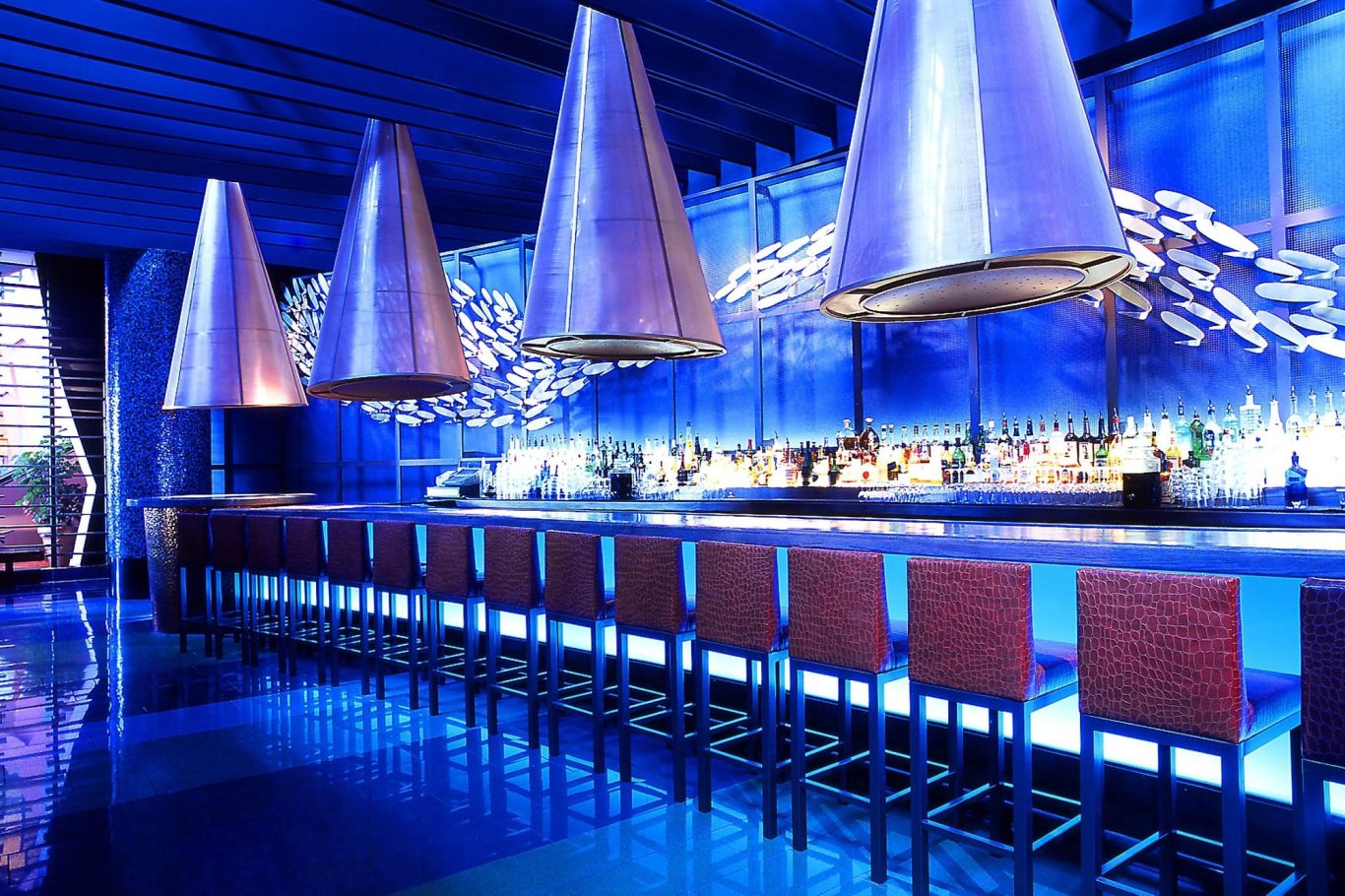 Sleek bar with blue lighting and modern pendant lamps, featuring high stools.