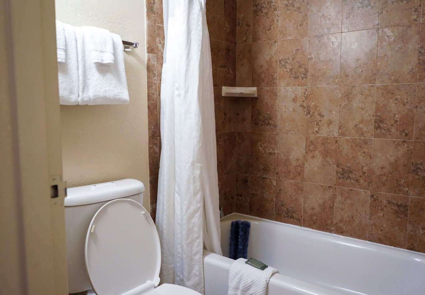 Clean bathroom with a bathtub, toilet, towels, and a shower curtain.
