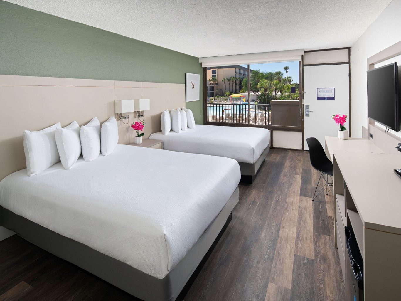 Modern hotel room with two queen beds, desk, and a view of the outdoors.